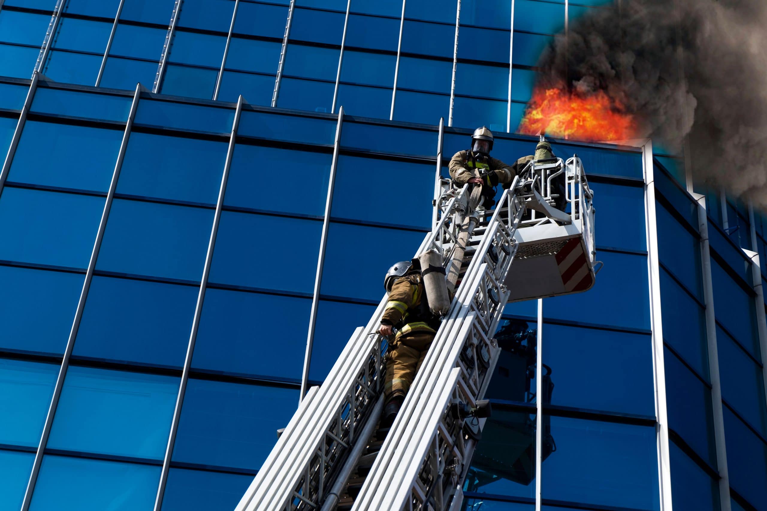 Firemen on ladder in front of tall building on fire.