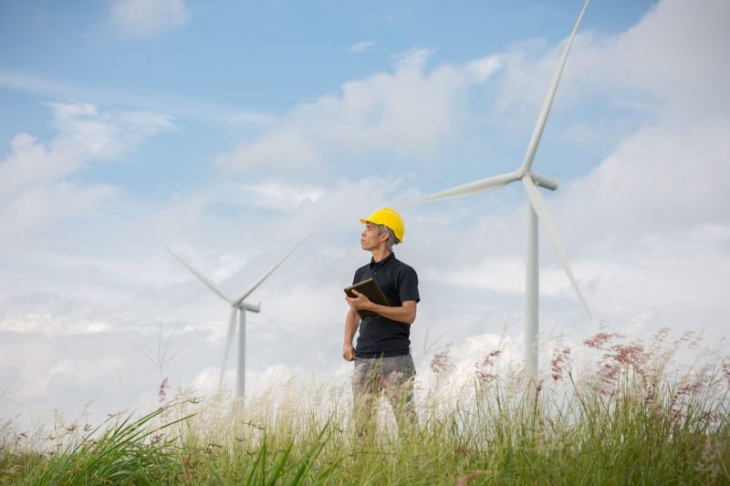 Man with hard hat standing in field of windmills.