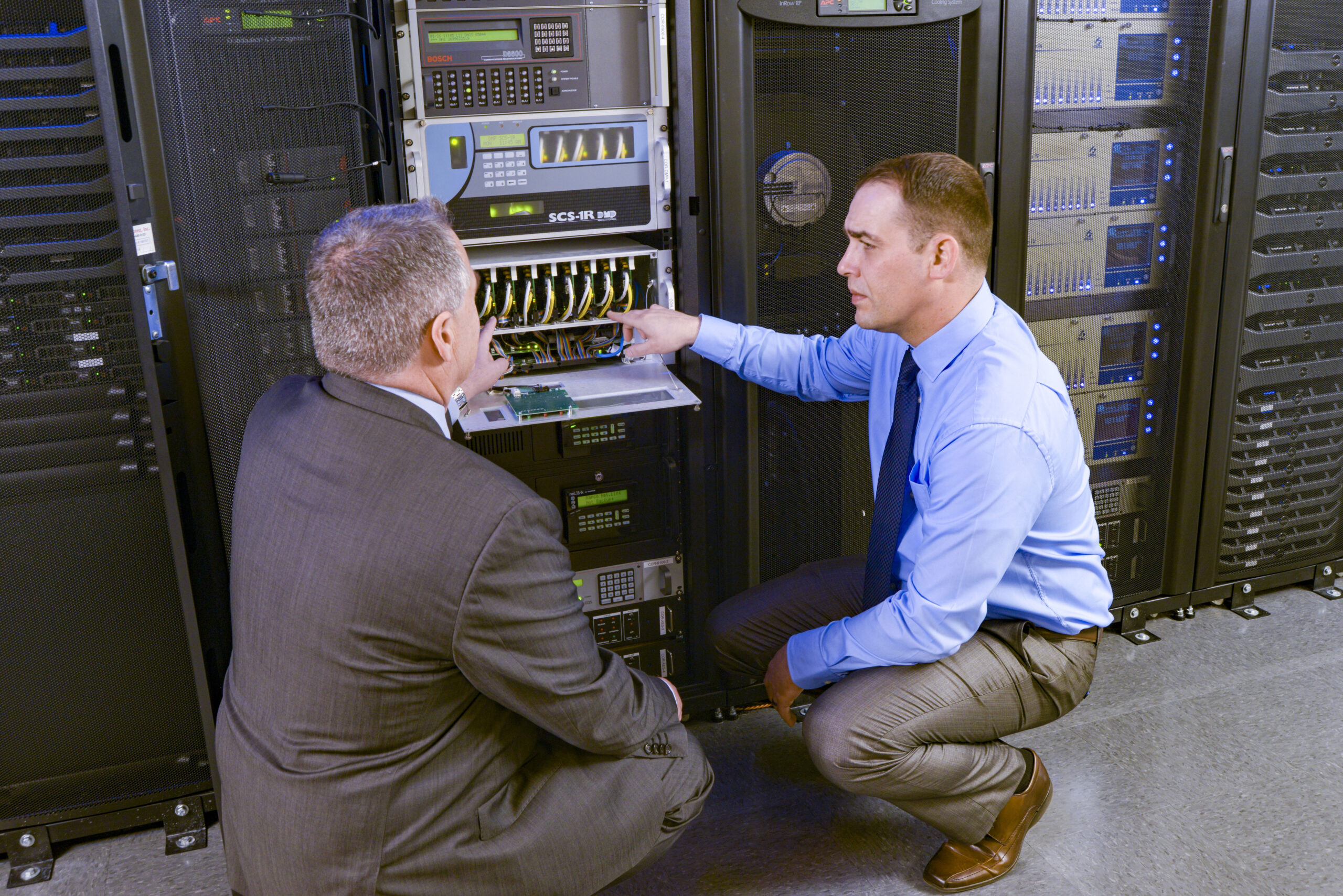 Two men discuss next to a computer.